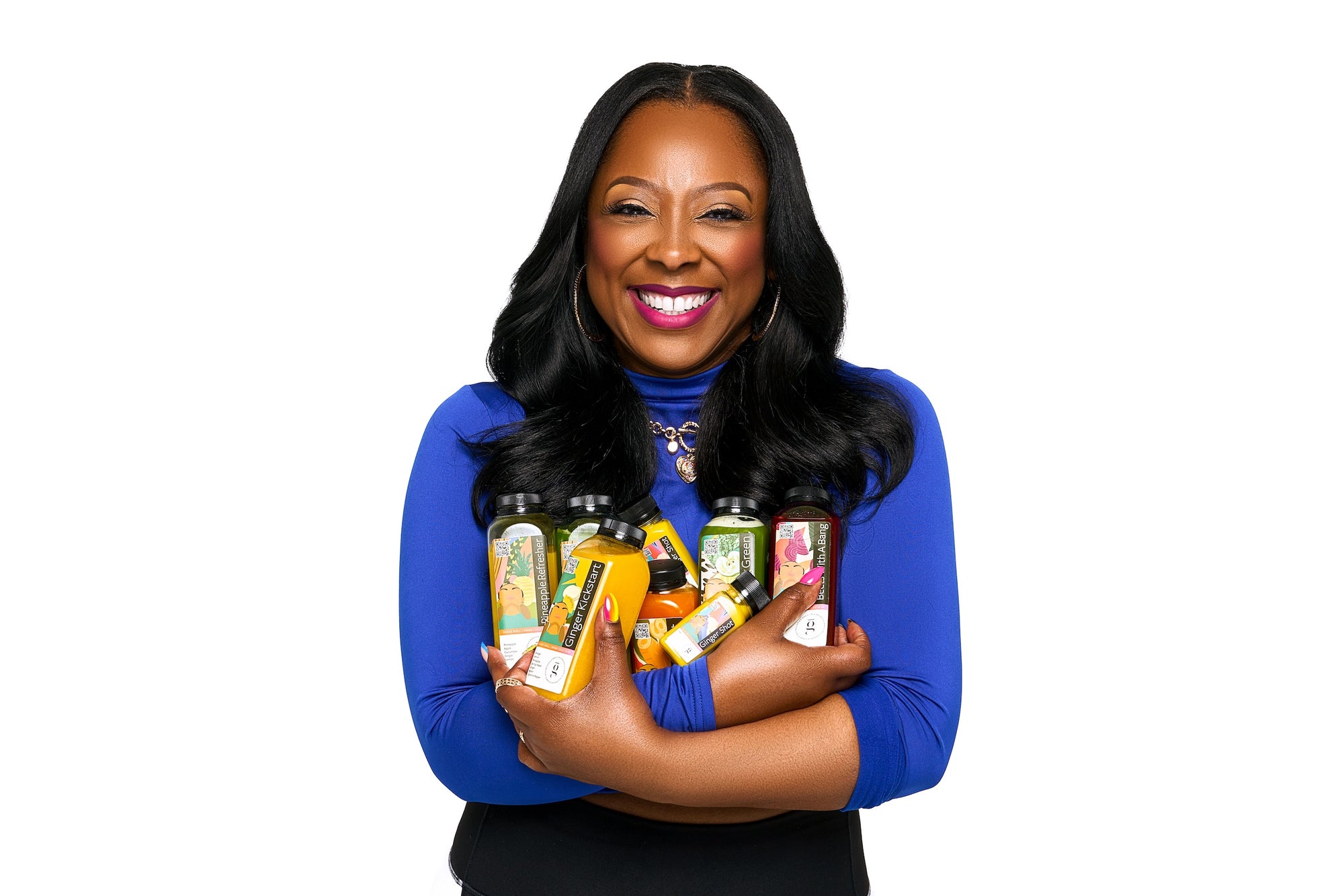 Black woman in royal blue shirt cradling eight cold press juices in her arms.