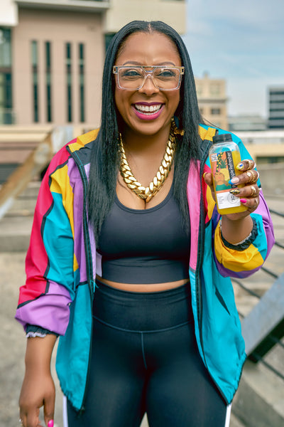 Black woman on roller skates in multi-colored jacket holding a cold press juice.  